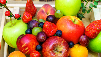 Set of berries and fruits in wooden box. Apple, strawberry, grape, berry and peach on a red brick background.
