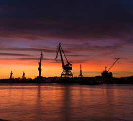 Fiery sunset and silhouettes of cranes at a wharf