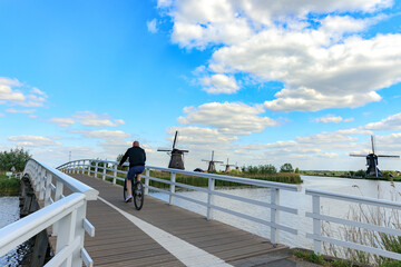 Outdoor sport, man rides a bicycle on old woden bridge, windmills in dutch landscape, Kinderdijk in South Holland, Netherlands