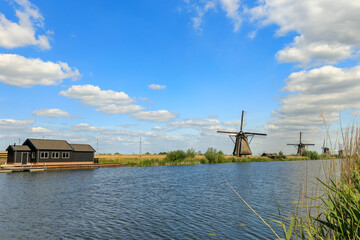 Dutch countryside, water, small river in field, windmills, green graas and blue cloudy sky, landscape in Kinderdijk, in the province of South Holland, Netherlands