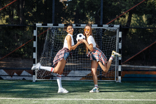 Two positive young teenage hipster girls posing with happy faces in front of goal post at the soccer stadium.