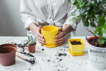 Young girl is engaged in gardening at home. The gardener girl is holding a yellow pot. Land and garden tools