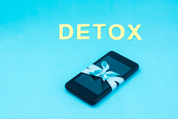 Digital detox concept. The smartphone is tied with a blue ribbon and the word detox on a blue background. Gadget addiction