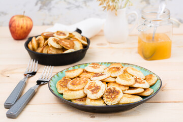 Trend breakfast. Dutch mini pancakes on a plate and a frying pan with them on a wooden table.