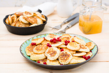 Trend breakfast. Dutch mini pancakes with red currants on a plate and a pan with them on a wooden table.
