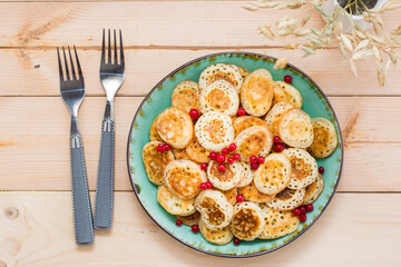 Trend breakfast. Dutch mini pancakes with red currants on a plate on a wooden table. Top view