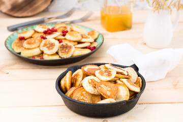 Trend breakfast. Dutch mini pancakes in a pan and on a plate with red currants on a wooden table.