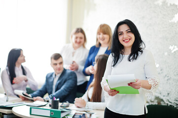 Portrait of caucasian woman in white blouse hold green folder against business people group of bank...