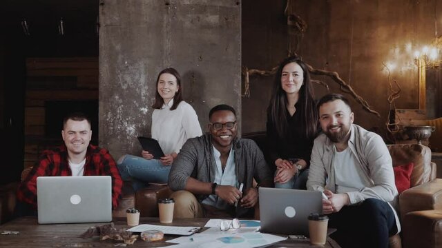 Dream team of casually dressed designers drafting together cooperating in good mood, young creative having meeting in modern loft office discussing ideas for startup project. smiling at camera