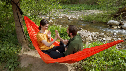 Loving couple sitting in hammock at the nature and playing interactive games. Enjoying life outdoor