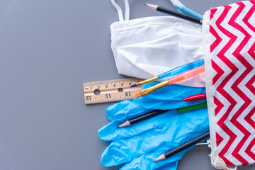 Close-up of child's pencil case with school supplies, medical mask, and surgical gloves spilling out onto desk