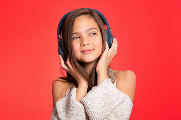 Girl in the headphones. Lovely European girl teenager 10 years old listens to music on headphones, relaxes, enjoys. Music lover since childhood. Music fan, DJ. Portrait on a red background.