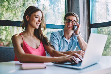 Cheerful young man and woman watching funny webinar on netbook in cafe