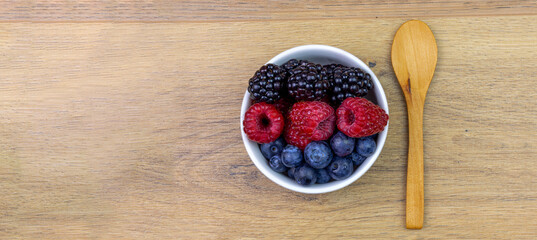 bowl with blackberries, raspberries and blueberries with wooden spoon on kitchen table, panorama