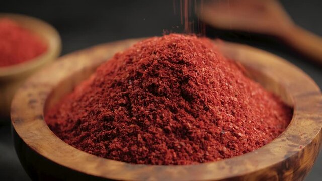 Red chili powder or paprika falling in a wooden bowl on a dark background, close-up. Cooking ingredients, flavor.