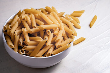 Raw dry uncooked penne pasta noodle in a bowl on white background 