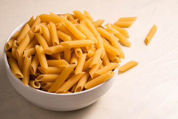 Raw dry uncooked penne pasta in a bowl on white background. Good for basil tomato pesto sauce Homemade fresh Italian food style bio organic whole wheat vegan spaghetti noodle for a healthy meal