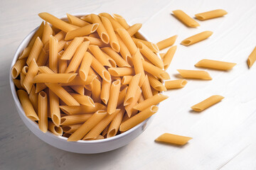 Raw dry uncooked penne pasta noodle in a bowl on white background 