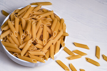 Raw dry uncooked penne pasta noodle in a bowl on white background 