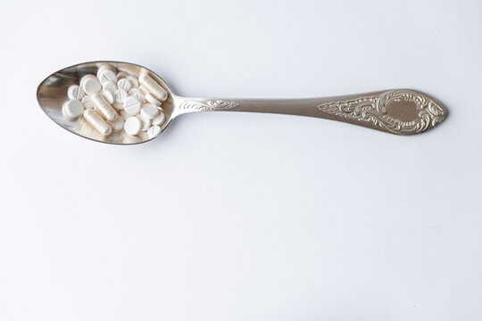 Medicine and health, treatment, pharmacy, coronavirus, pandemic, epidemic concept - layout one silver big tablespoon with different pills and capsules on a white background copy space.