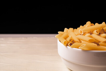 Raw dry uncooked penne pasta noodle in a bowl on white background 