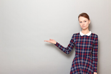 Portrait of serious girl pointing with one hand at copy space