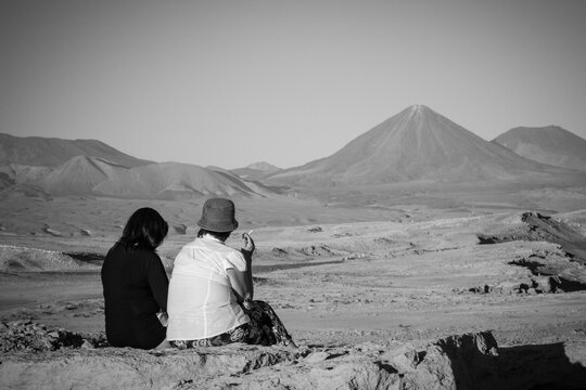 Duas mulheres de costas fumando um cigarro e contemplando a paisagem seca do deserto do Atacama, Chile.