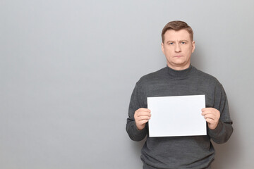 Portrait of serious man holding white blank paper sheet in hands