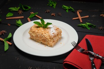 Homemade cake Napoleon with mint, decorated with cinnamon. On a white plate. On black background