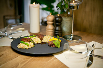 beef Medallions with bulgur and asparagus. On a black plate. Against the background of a restaurant