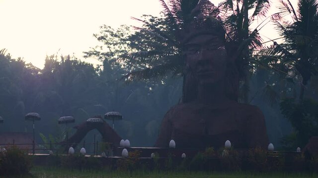 Traditional Balinese large bamboo statue overlooking rice paddy fields at sunrise