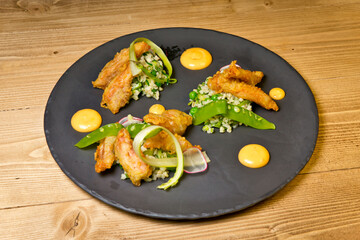 Grilled octopus tentacles with rice and vegetables. On a black plate. On a rustic wooden background