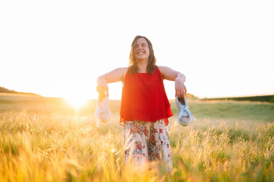 Young playful woman, laughing while throwing sneakers in the meadow at summertime sunset. High quality photo .