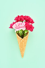 Red carnation flowers in waffle ice cream cone on green background. Summer concept. Top view
