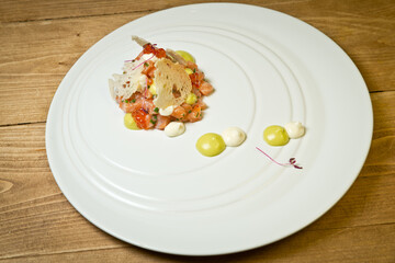 Salmon tartare with red caviar and croutons .On a white plate. On a rustic wooden background