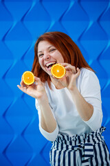 Girl on a bright blue background in a white blouse with oranges in hand