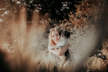 Obraz premium Junges Mädchen mit einem Hund auf dem Arm steht im Feld