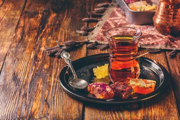 Tea in armudu glass with oriental delight rahat lokum on metal tray over wooden surface and...