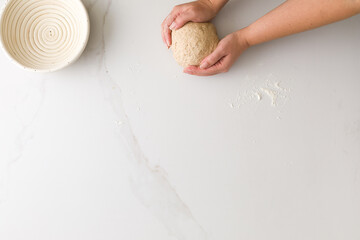 Top view of female hand molding bread dough in a marble table with an empty bread bowl with space for text