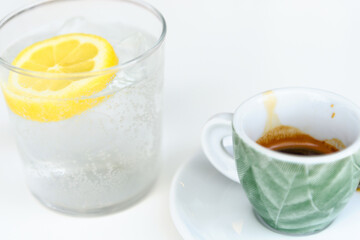 Glass of sparkling water with lemon and cup of coffee. Iced mineral water with lemon and cup of coffee on the white table.