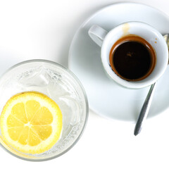 Glass of sparkling water with lemon and cup of coffee. Iced mineral water with lemon and cup of coffee on the white table.