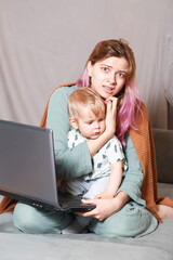 A young woman works at home with a laptop, along with a child.the son wants to communicate with his...