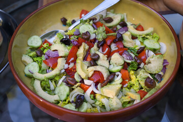 Fresh salad with avocado, olives, tomatoes and other healthy ingredients in a rustic bowl