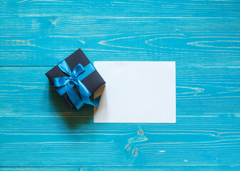small gift box with blue ribbon and signature card on aquamarine wooden background, top view