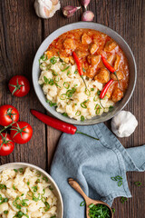 Hot pork goulash with chili, tomato and pepper, served with boiled dumplings topped with spring onion greens