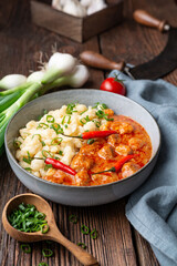 Hot pork goulash with chili, tomato and pepper, served with boiled dumplings topped with spring onion greens