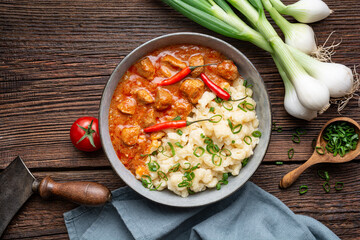 Hot pork goulash with chili, tomato and pepper, served with boiled dumplings topped with spring onion greens