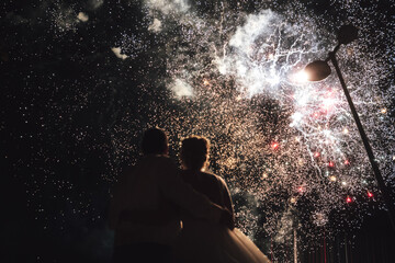 Rear view of couple watching amazing huge fireworks. Newlyweds embracing and enjoying their wedding celebration.