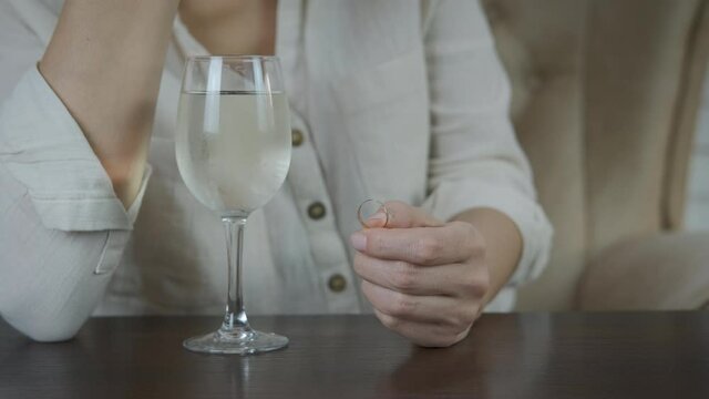 Betrayal in family. A woman throws a wedding ring into a glass of wine.