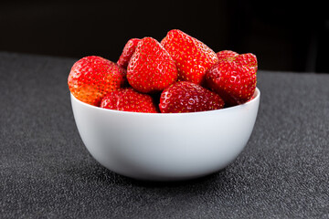 A lot of fresh strawberries in a white vase on a black background close-up
